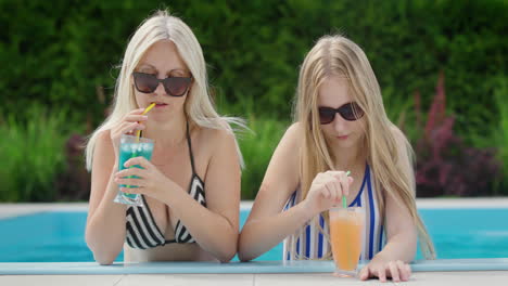 mom and teenage daughter relax by the pool, drinking cocktails