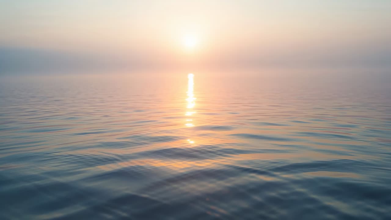 Brightening low sun rising above horizon, causing reflection shifting on calm ocean with ripples