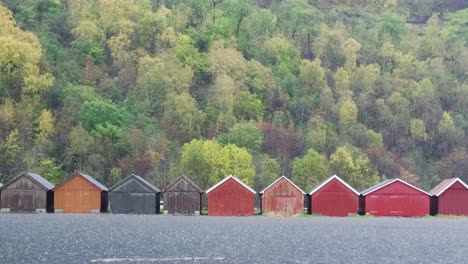 row of traditional norwegian rorbuer cabins in the rain with autumnal trees in background