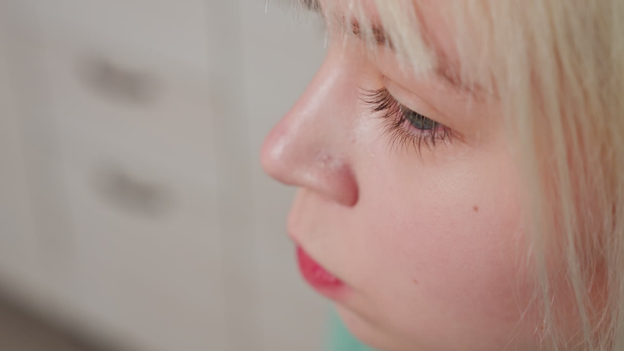 extreme close up of lady savoring chip in kitchen setting with cabinet blurred by side, detail on lips, nose, fair skin, blond hair, enjoying snack, home environment, casual relaxed moment