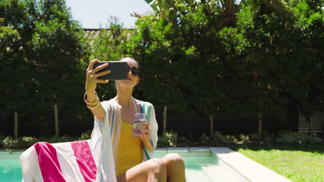 relaxing by pool, woman in sunglasses enjoying drink and using smartphone, copy space
