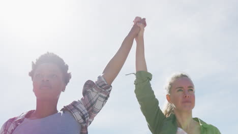 diverse female gay couple raising and holding hands at the beach