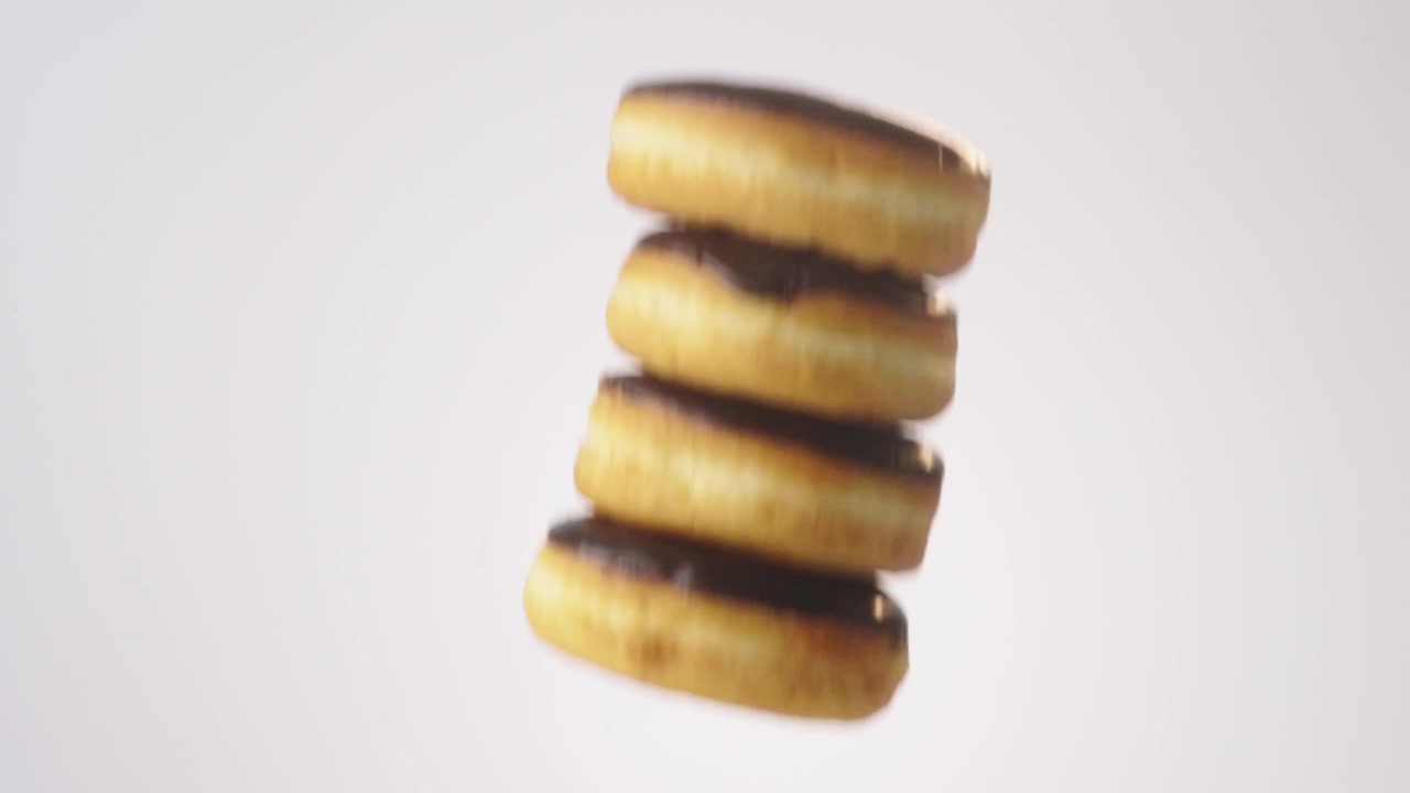 Chocolate-glazed glossy donuts cascading and falling through frame on white in slow motion. kids party content, birthday celebration posts, bakery counter videos.