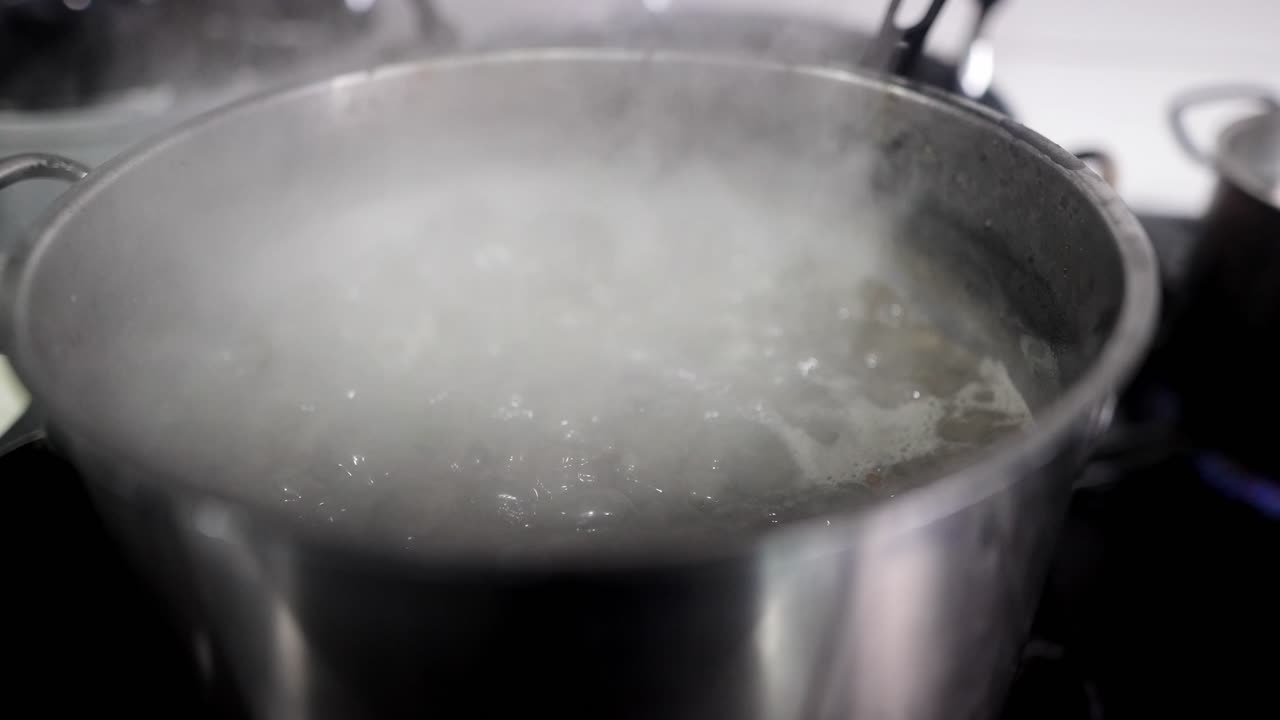 Close up view in slow motion of a pot with boiling smoky pasta water in a restaurant.