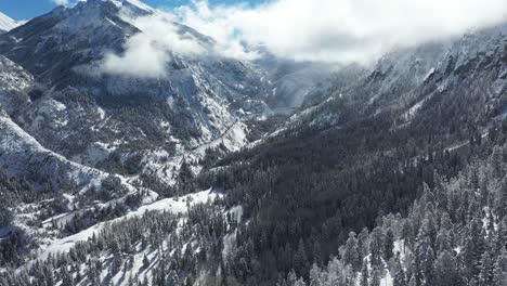 Vista-Aérea-Del-Idílico-Paisaje-Montañoso-De-Invierno,-Picos-Nevados-Y-Bosque-De-Coníferas-En-Un-Día-Soleado