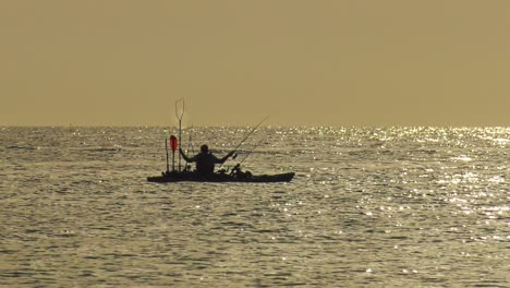 woman sea fishing from a kayak on calm sea at dawn, silhouette slow motion