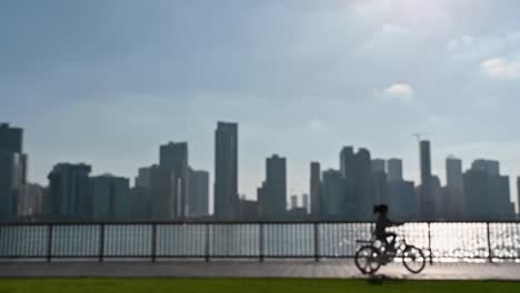 slow-motion, out of focus: a girl riding a bike, having fun outdoors with a city view in the background at khalid lake in sharjah, united arab emirates