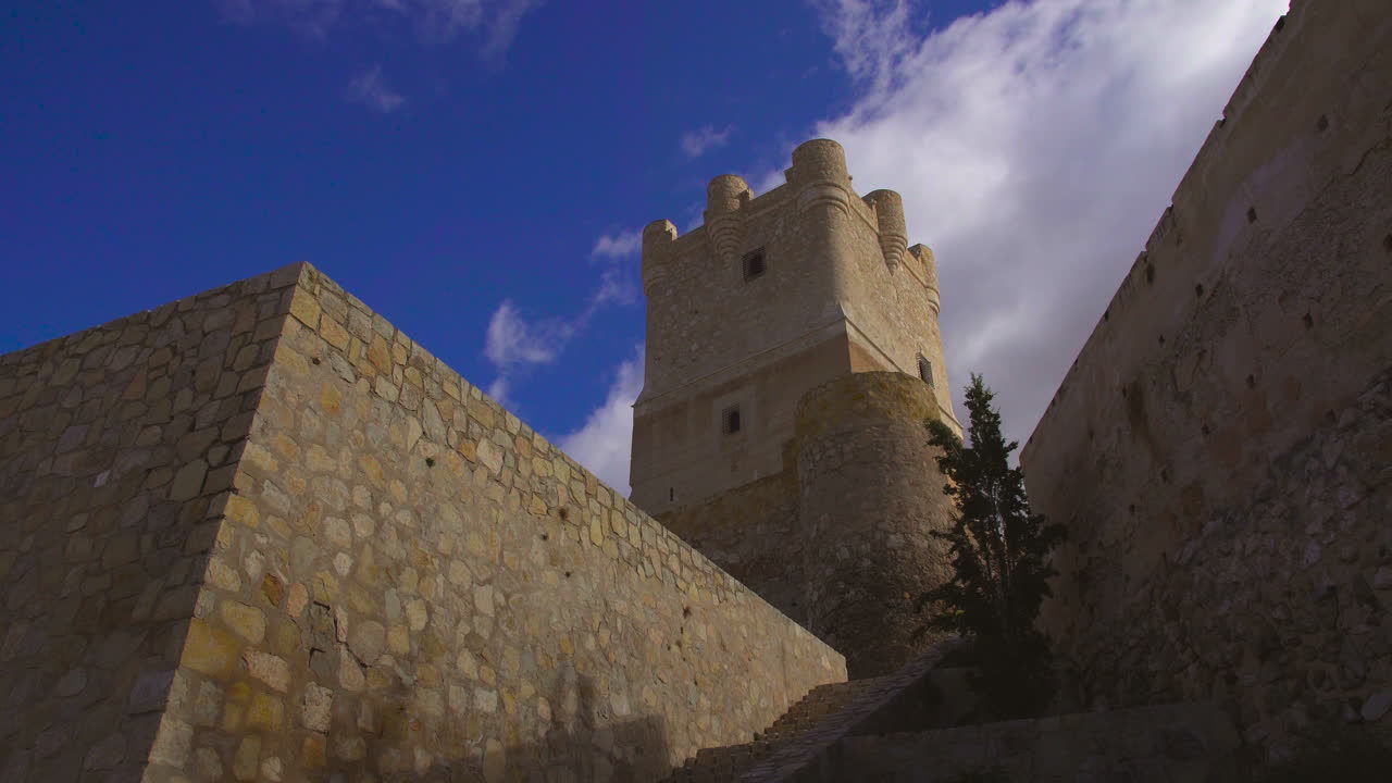 Low angle view of The Atalaya Castle where clouds are moving under the blue sky, Villena, Province of Alicante, southern Spain.
