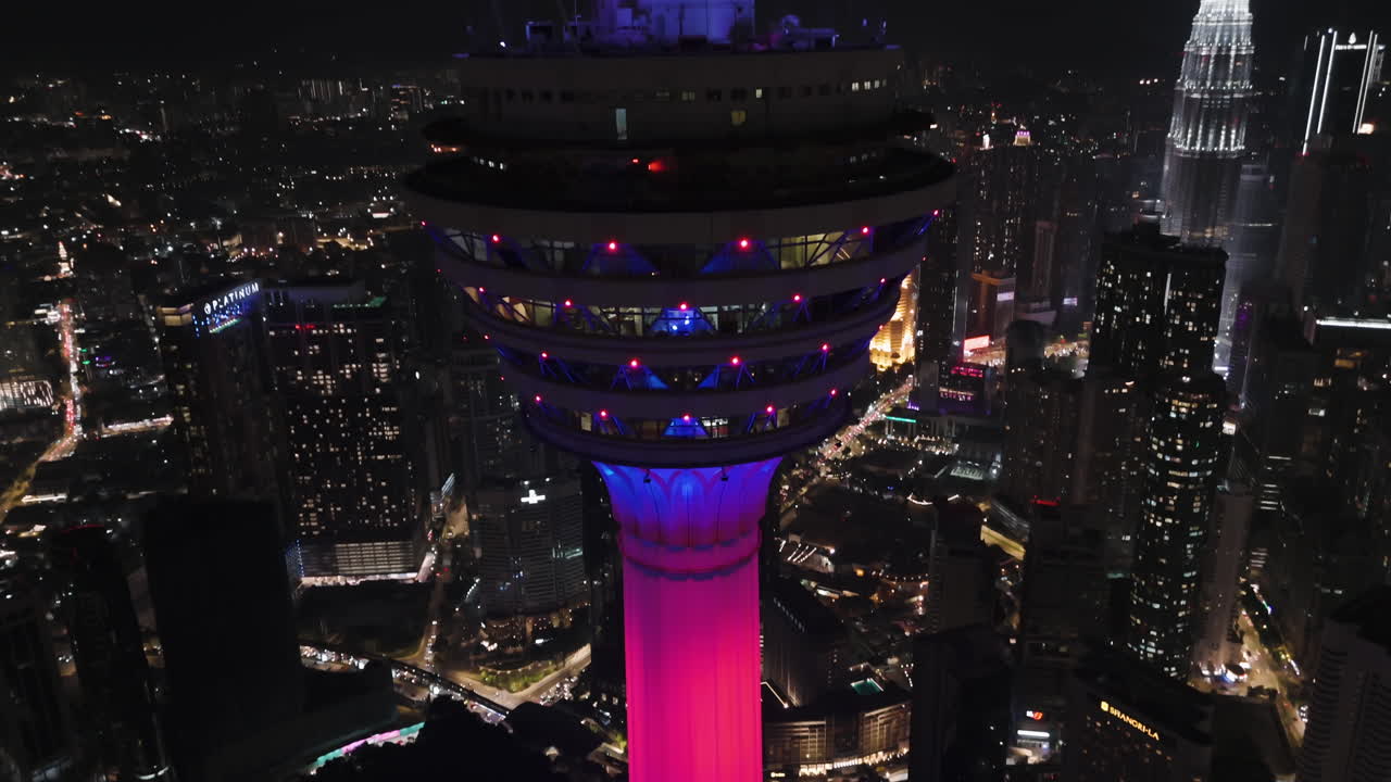 Drone diving down and tilting away from the night lit KL Tower, in Malaysia