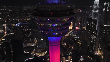 drone diving down and tilting away from the night lit kl tower, in malaysia
