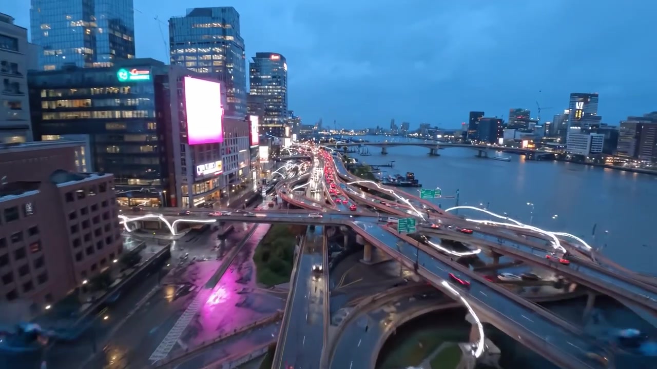 Aerial view of a modern urban cityscape at dusk, showcasing illuminated skyscrapers, busy highways, and reflections on wet roads beneath a cloudy sky.