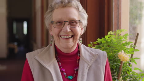 portrait-of-happy-elderly-woman-standing-by-window-laughing-cheerful-enjoying-retirement