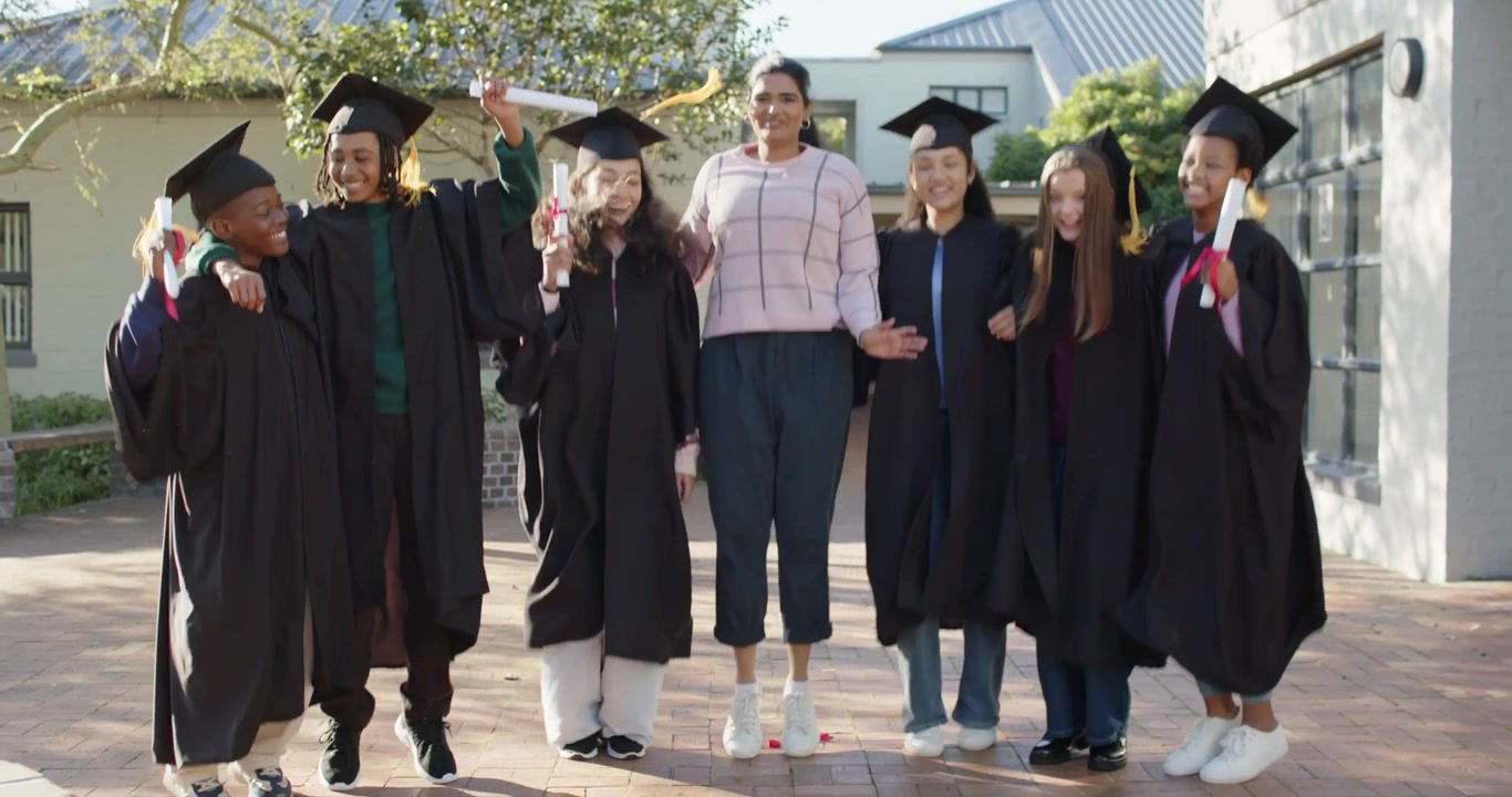 Amici di diverse etnie nel campus, al centro che si tengono a braccetto con un top rosa, che sollevano i diplomi, saltando e festeggiando.