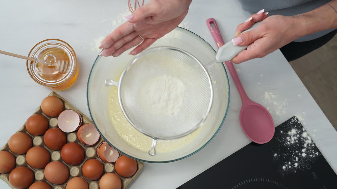 Woman cook pouring flour with a sifter into a bowl to make pancakes.