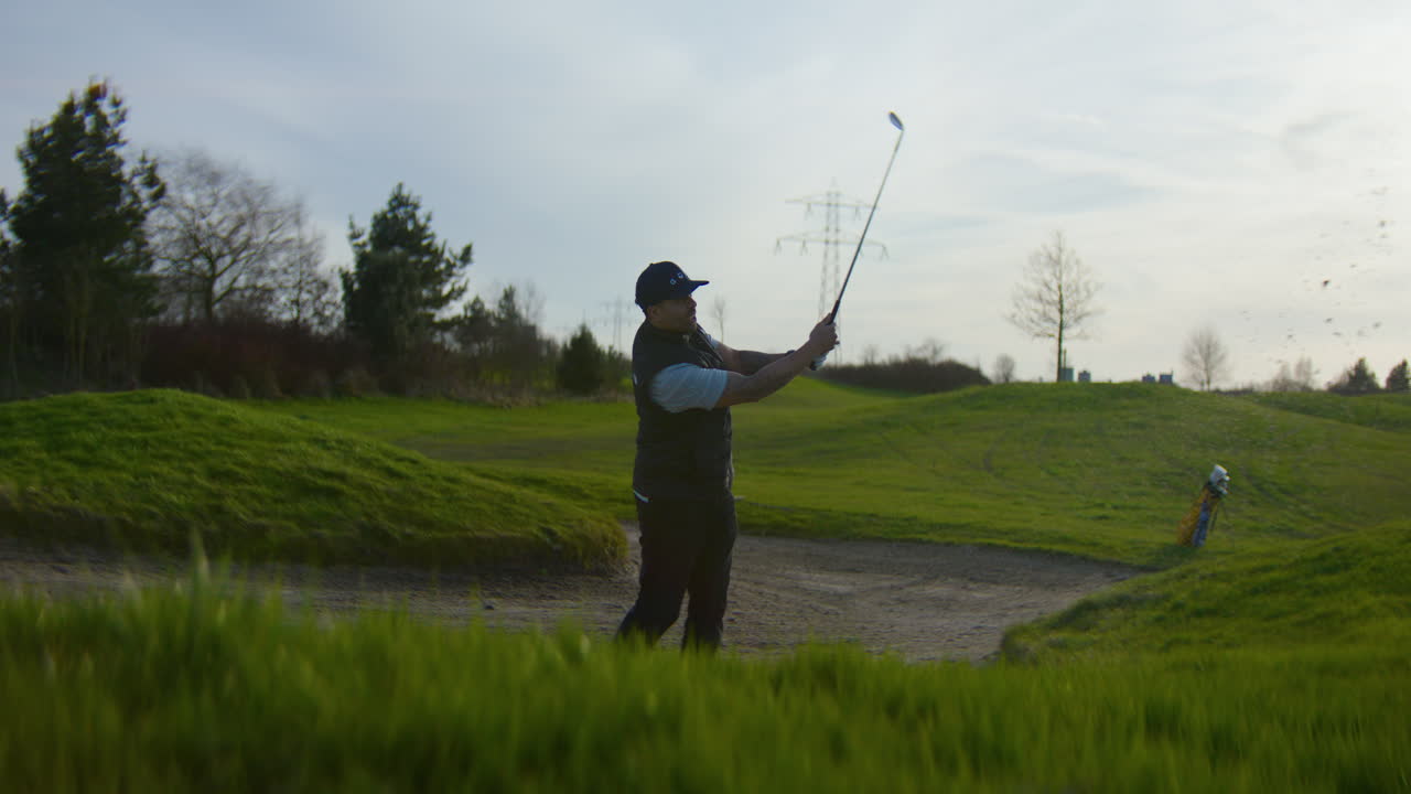 Golfer in bunker making great shot on golf course at sunset. Low POV, dolly right
