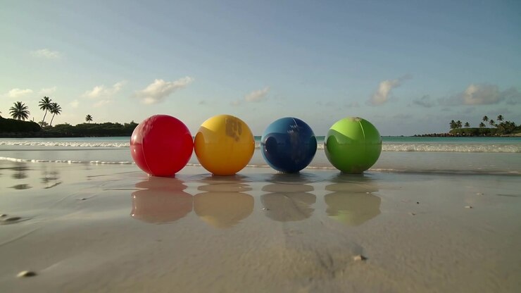 Bobbing four large plastic beach balls rocking on wet sand, incoming wave washing lower halves