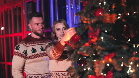 young couple decorates a christmas tree. happy guy and a beautiful girl getting ready for new year winter holidays celebration. festive mood in a modern cozy home