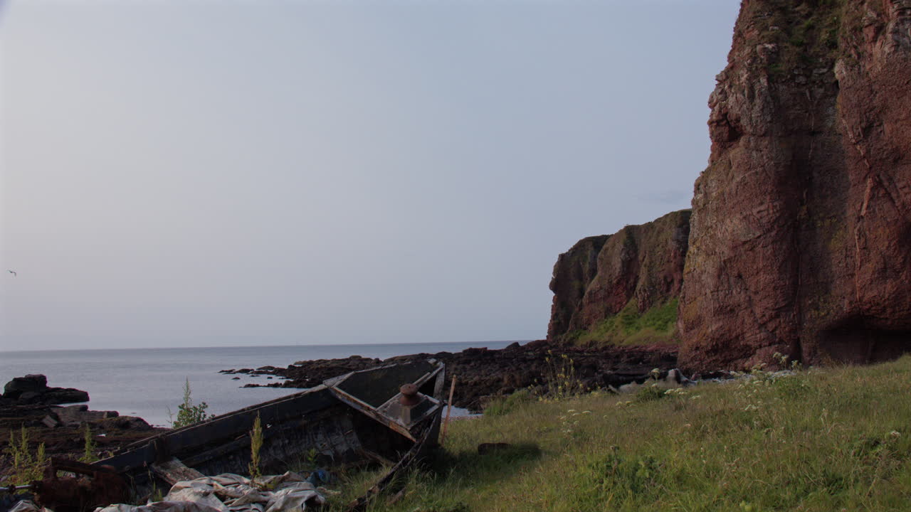 Wide shot of an abandoned derelict broken boat and cliffs at the old harbour at low tide at Auchmithie