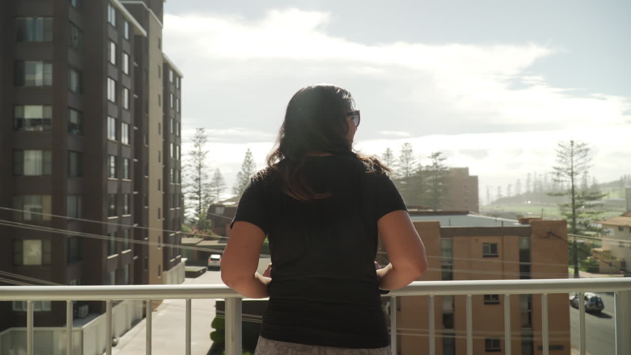 mujer india sudafricana de pie y apoyada en el balcón del apartamento disfrutando de la vista de la ciudad de port macquarie en nueva gales del sur, australia