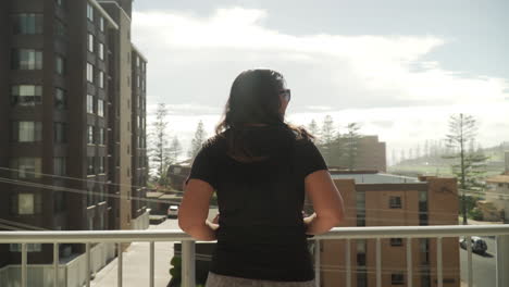 south african indian woman standing and leaning on the balcony of apartment enjoying the view of port macquarie town in new south wales, australia