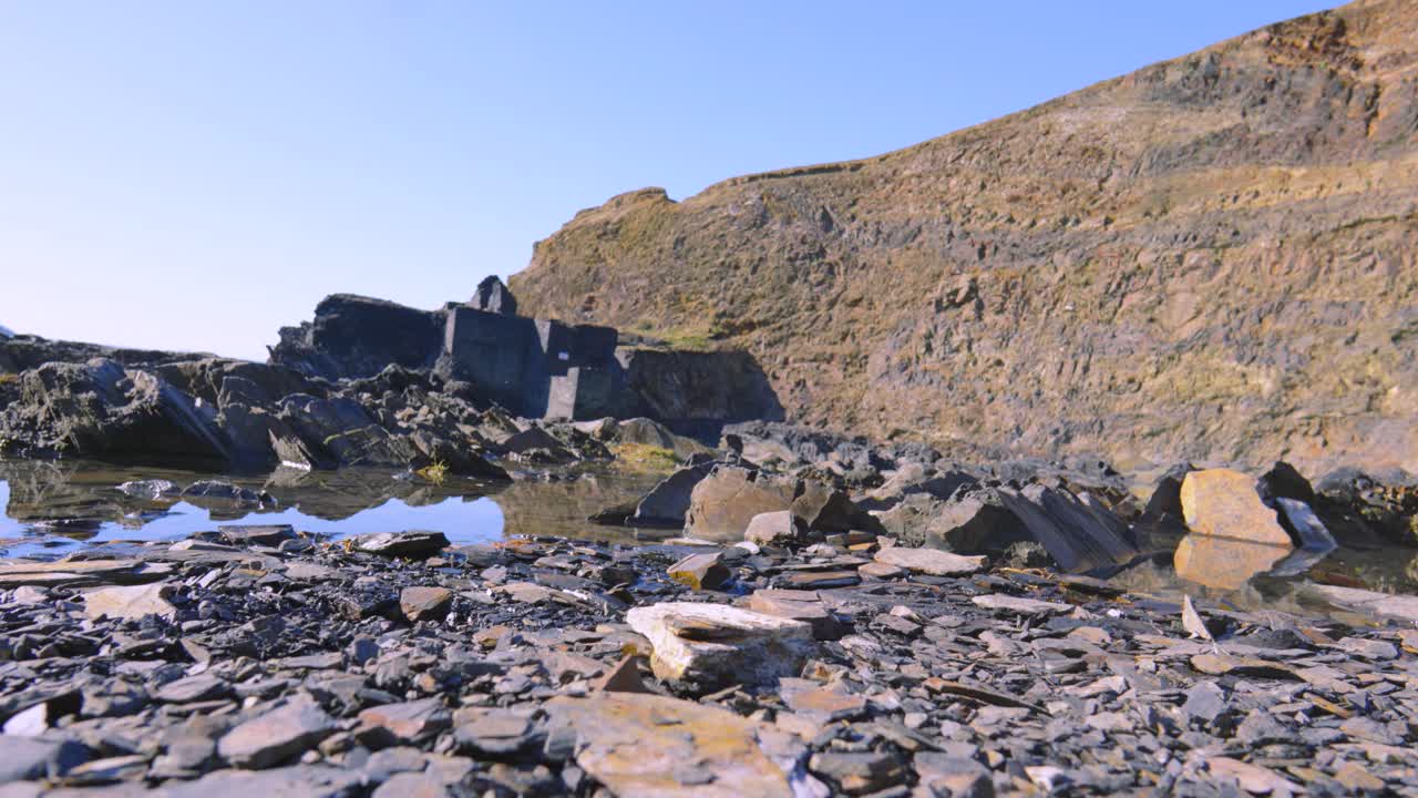 Slow Rising Shot of Abandoned Quarry with Historic Building in Background Near Beach with Sheer Cliffs Used for Excavating Raw Materials for Buildings.