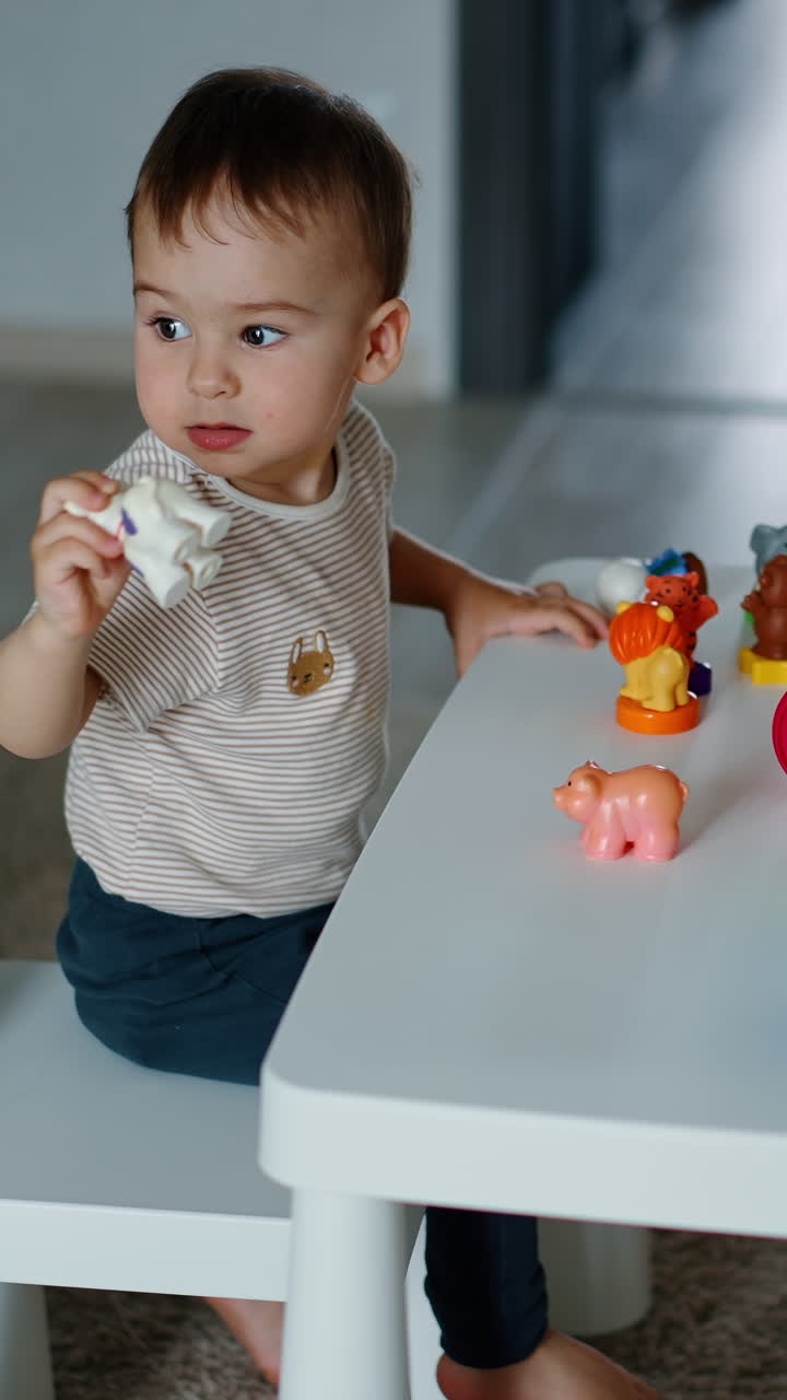 Beautiful toddler sits at little table playing with toys. Baby studying animals and colors. Vertical video