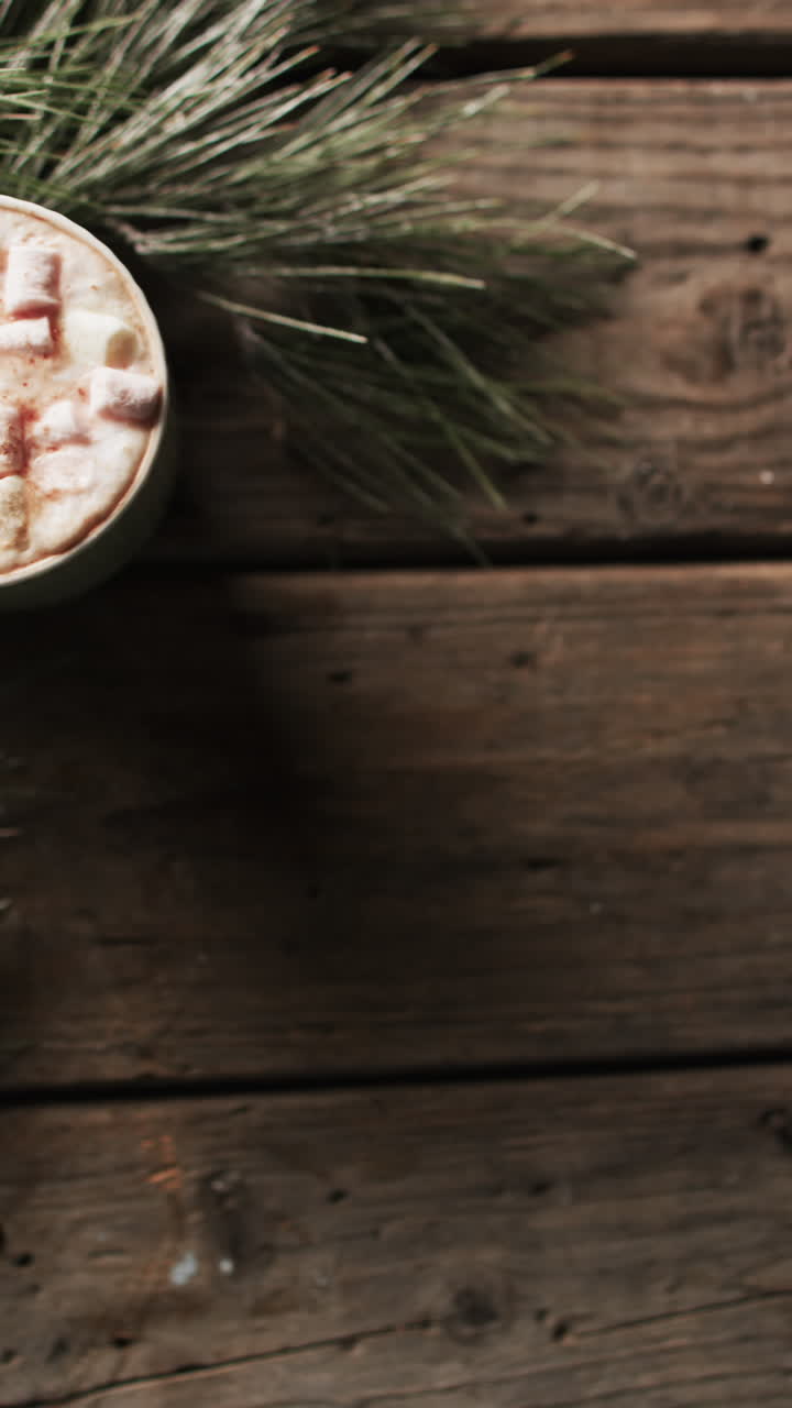 Vertical video of mug of chocolate, marshmallows, decorations and copy space on wooden background