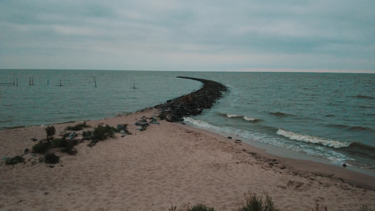 высокое до низкого видео, глядя на колыбель в озере, в то время как волны врезаются в пляж и колыбели