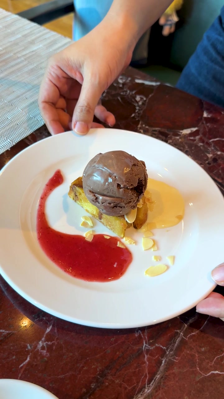 A server places a plated chocolate brownie with ice cream and strawberry sauce on a table