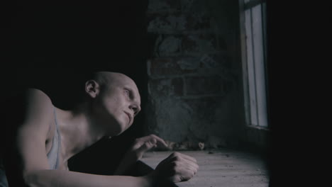 pale bald skinny man looks through the window in the creepy old bathroom at night
