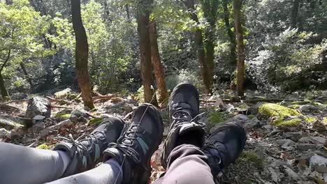 voeten van een wandelaarpaar rustend op rotsachtige grond in diep bos op een zonnige vroege herfstdag, deel 2, pan rechts