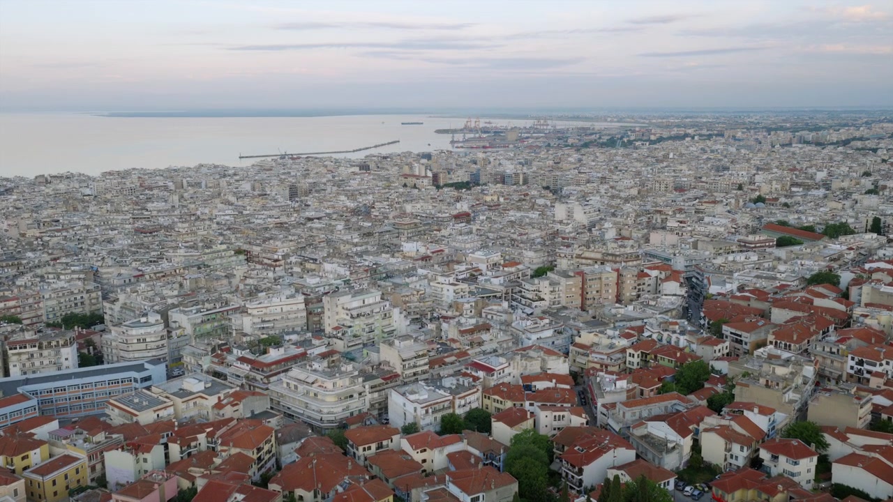 Ampia panoramica aerea di Salonicco, che mostra l'espansione urbana, il porto e la costa del Golfo Termaico sotto un cielo velato