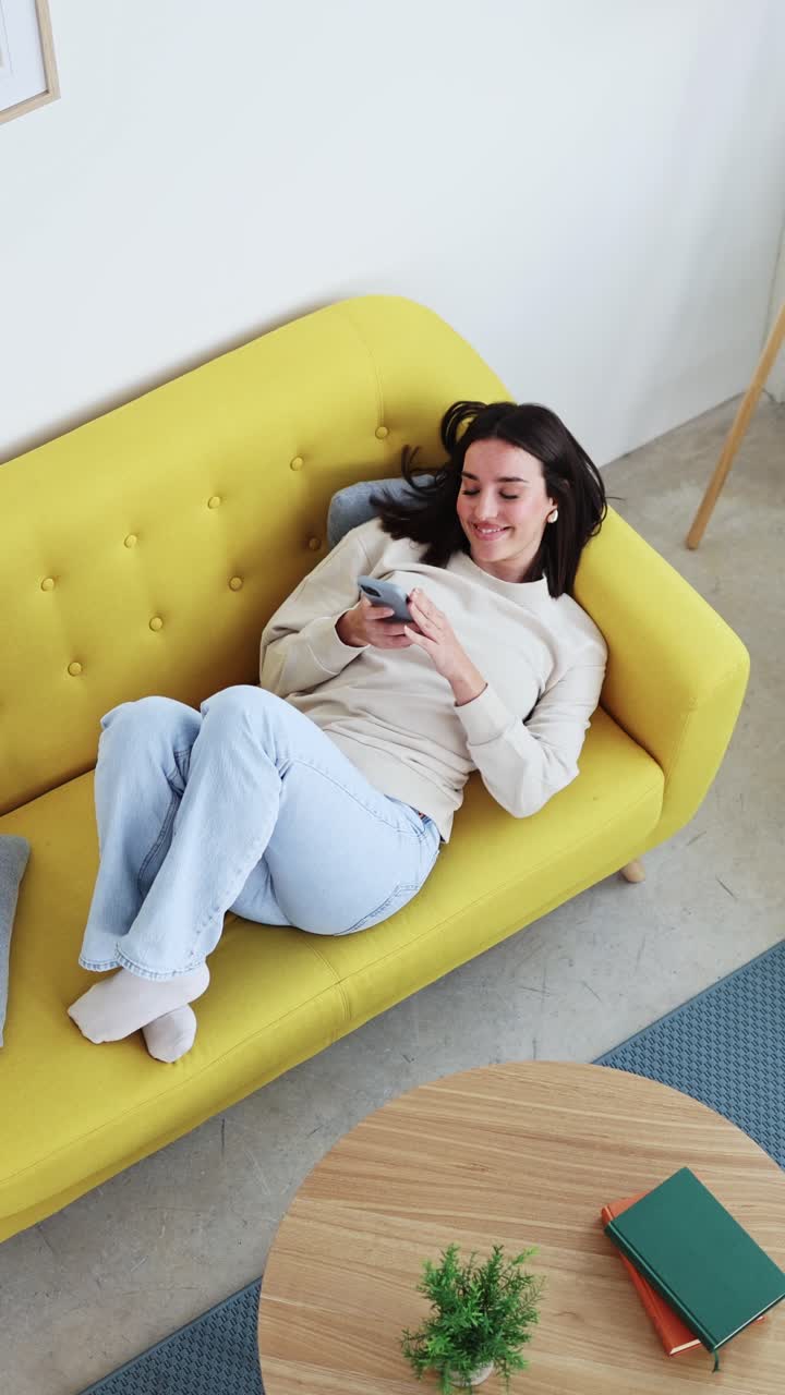 Giovane donna che si rilassa su un divano giallo e usa lo smartphone