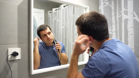 Man-shaving-beard-using-electric-shaver-in-bathroom,-clean-face