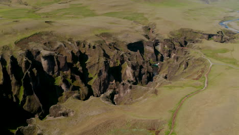 Top-down-view-panorama-of-Fjadrargljufur-canyon,-a-100-meters-deep-gorge-in-south-Iceland.-Drone-view-of-majestic-rock-formation-caused-by-erosion-of-Fjadra-river-flowing-through-it