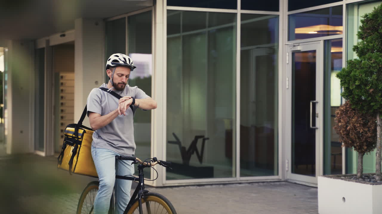 Food Delivery Guy Wearing Thermal Backpack Takes A Look At His Smartwatch To Know Where To Go With His Bike