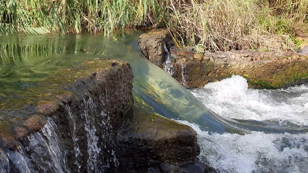 A torrent of crystal clear mountain water flowing through and over an old stone weir
