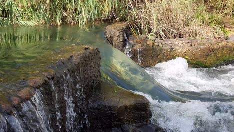 a torrent of crystal clear mountain water flowing through and over an old stone weir
