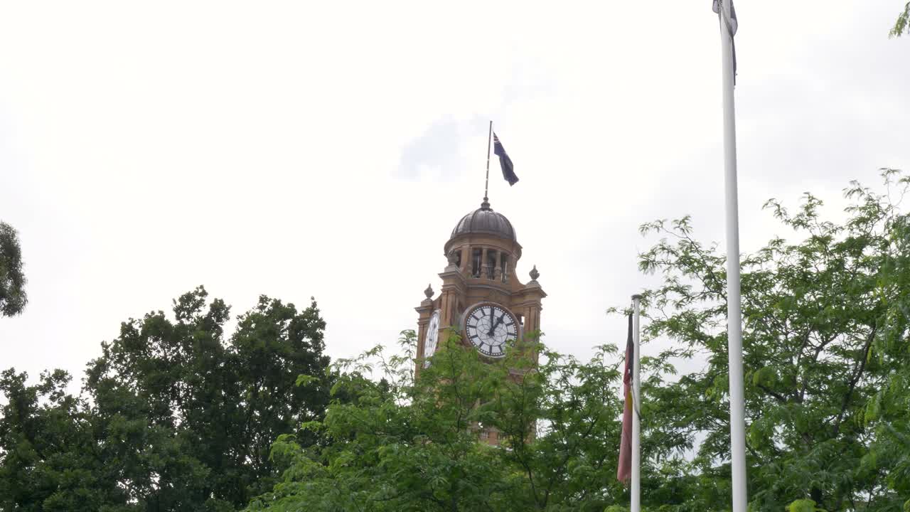 Slow motion landscape of the Australian flag waving in the wind on top of the historic Central Station clock tower building landmark with trees in the foreground Haymarket Sydney NSW Australia tourism