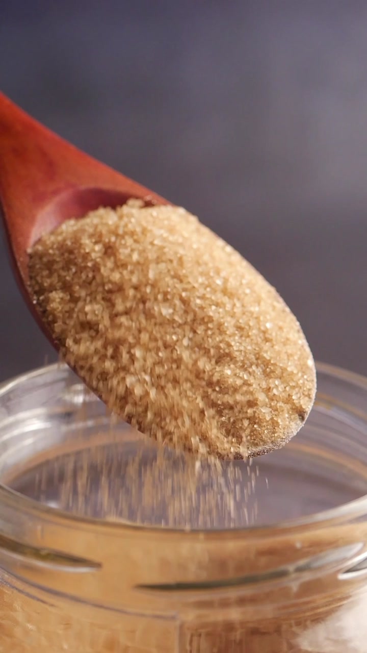Brown Sugar Pouring from a Wooden Spoon into a Glass Jar