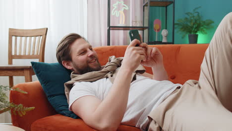 Portrait-of-young-man-lying-on-couch,-using-smartphone-share-messages-on-social-media-application