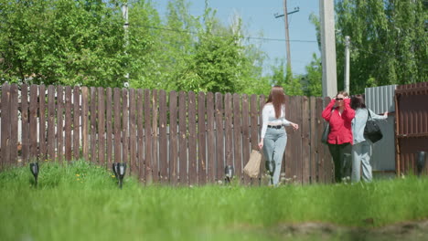 young girls return home after shopping, visible only through shadow cast on metal gate, brown and wooden fences surround grassy yard, small black lamps aligned beside concrete path