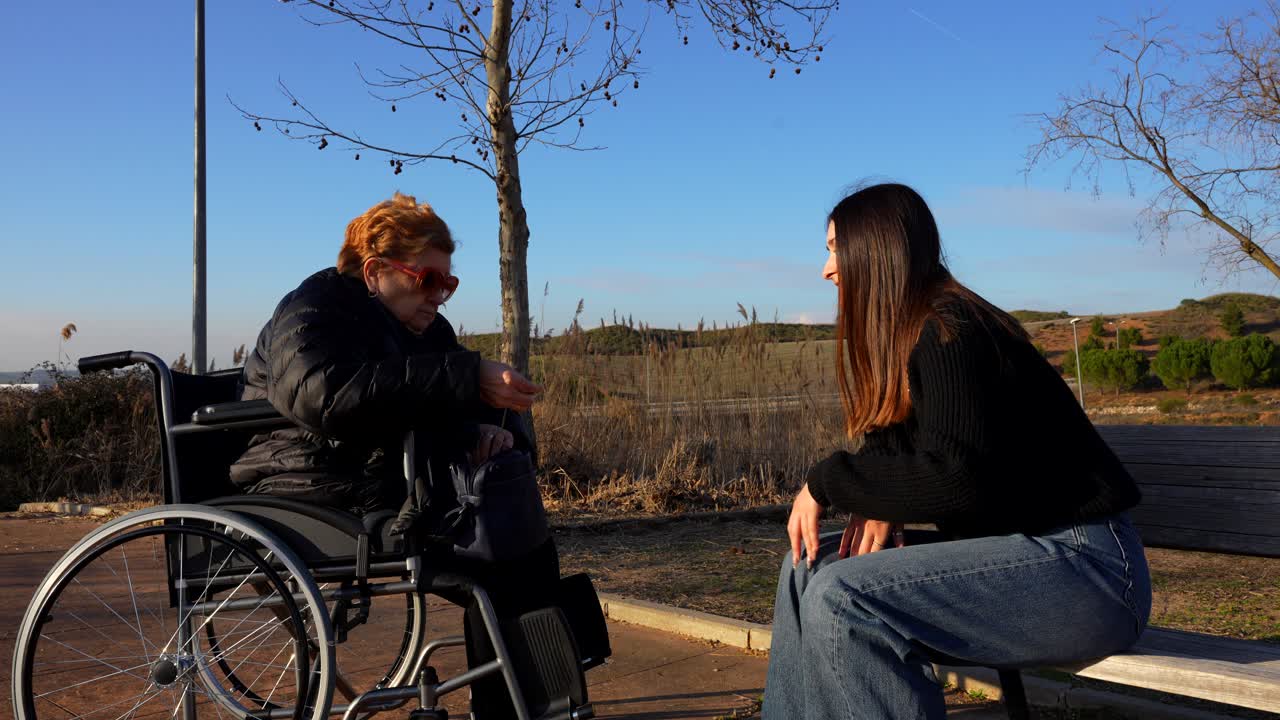 Elderly woman in wheelchair talks with granddaughter while looking inside her bag