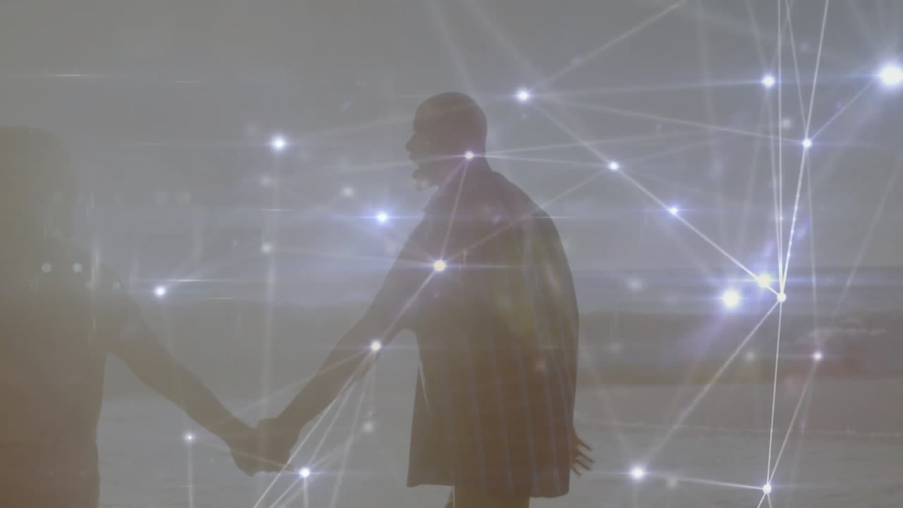 Mature man and senior woman holding hands on beach, showing tech network overlay connecting nodes