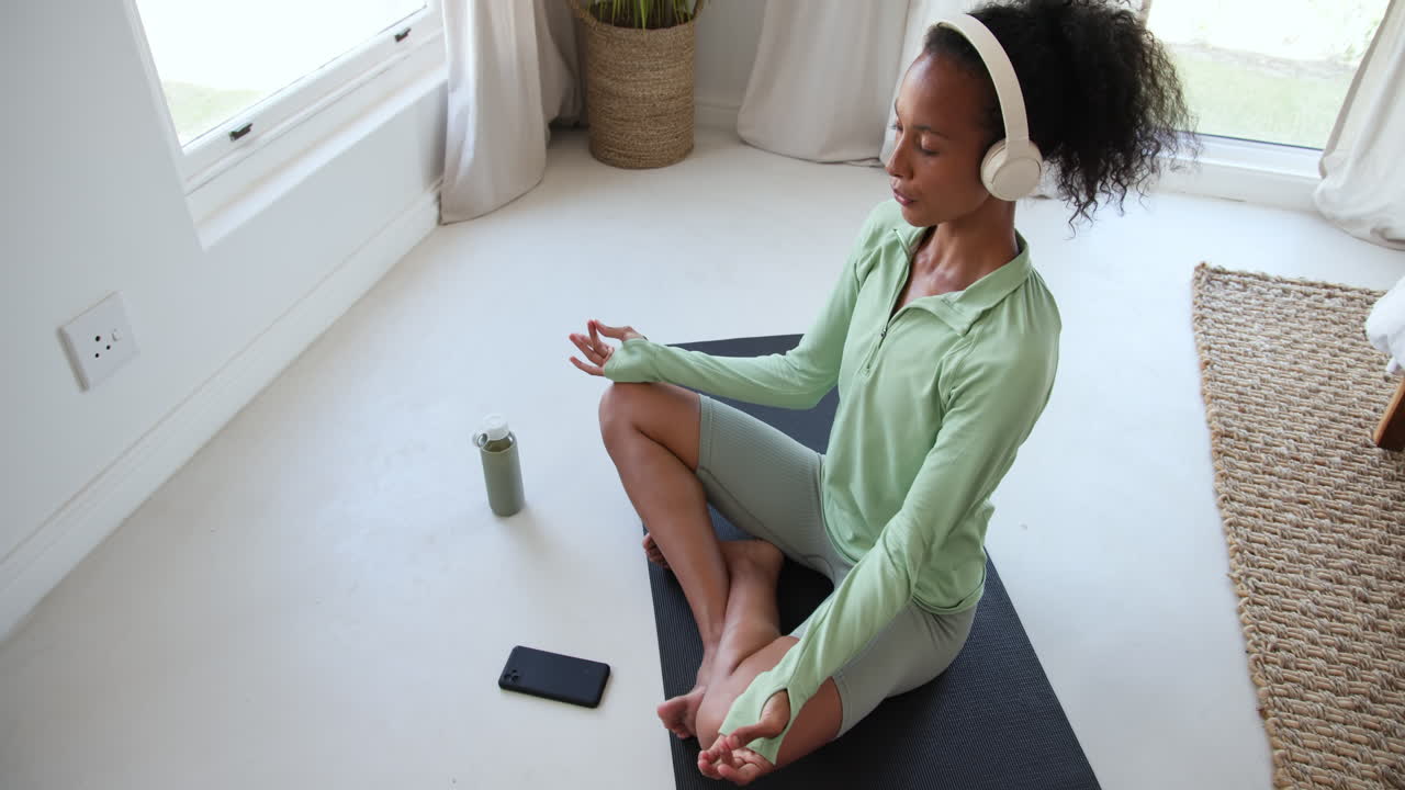 Meditating at home, woman in activewear with headphones stretching on yoga mat
