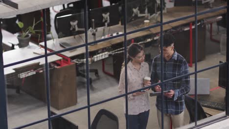 two happy diverse creative designers in discussion at tablet in casual office, slow motion