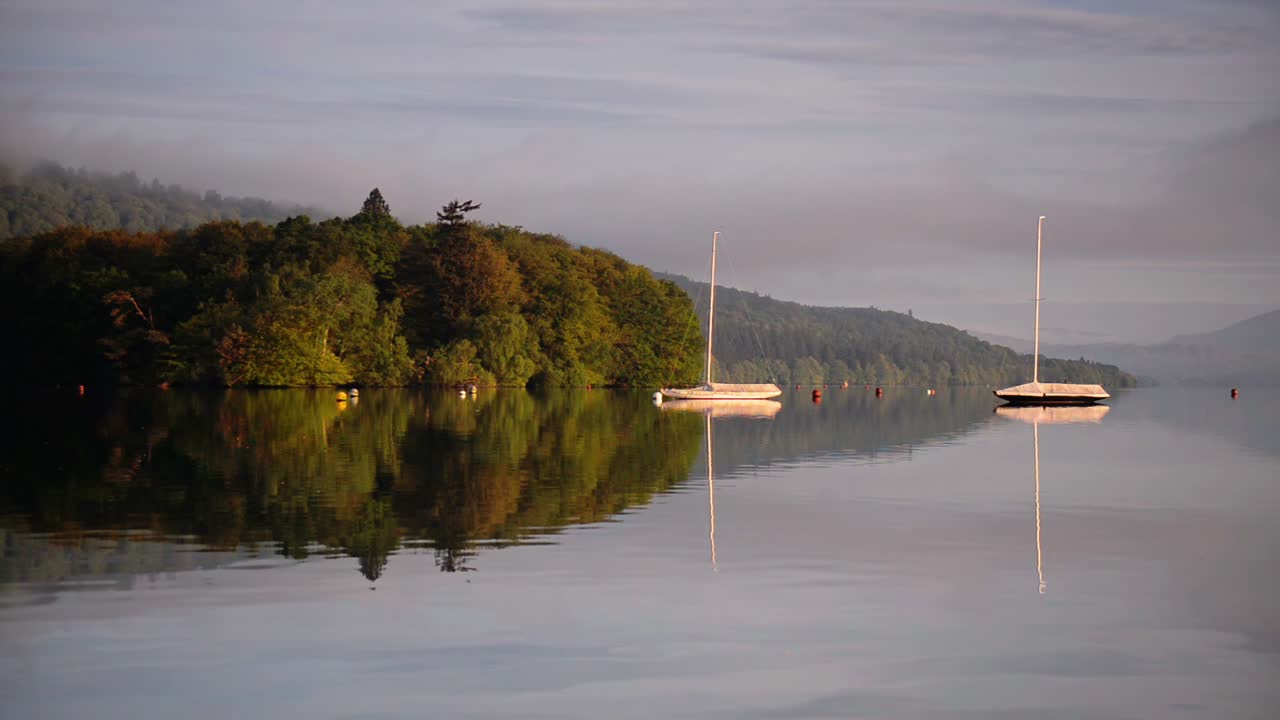 Two Boats Anchored In Lake District With Lush Green Mountains On the Background Perfectly Reflecting On The Water In London, England, UK.- wide shot