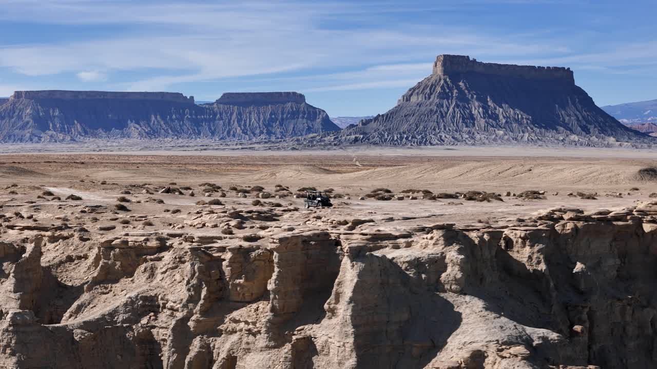 Vista aérea de un vehículo todoterreno negro circulando cerca de los acantilados de una mesa en el paisaje desértico y seco de Utah, EE. UU.