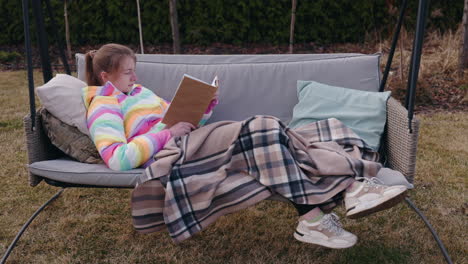 teenage girl reading a book on a garden swing