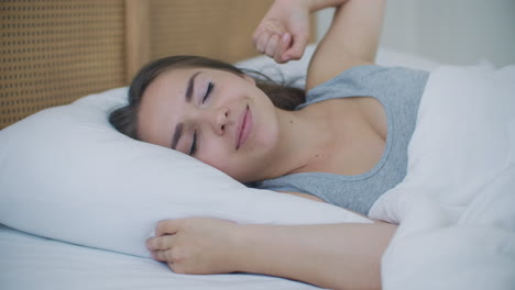 young woman wakes up in bed in the morning smiling raises her hands